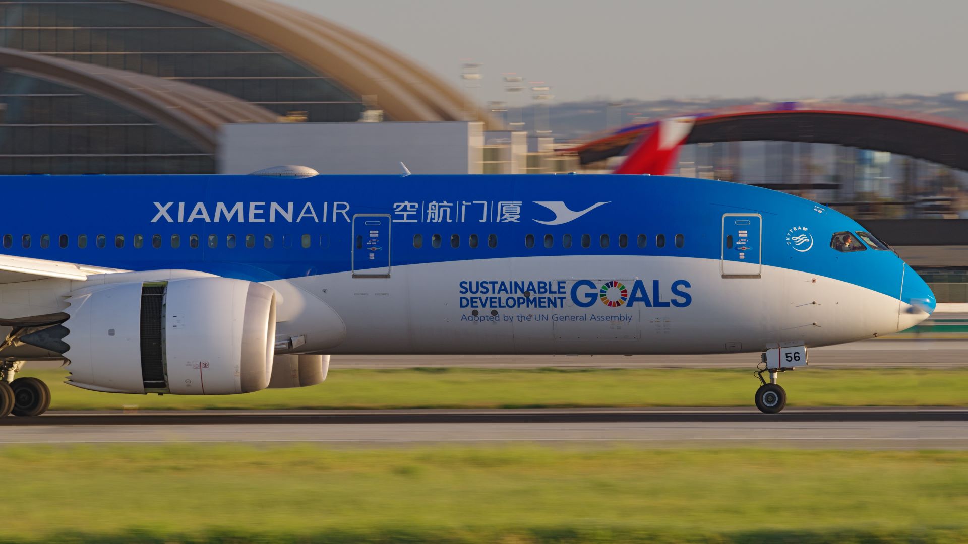 A bright blue Xiamen Airlines plane, front half-view, landing on runway in Los Angeles.