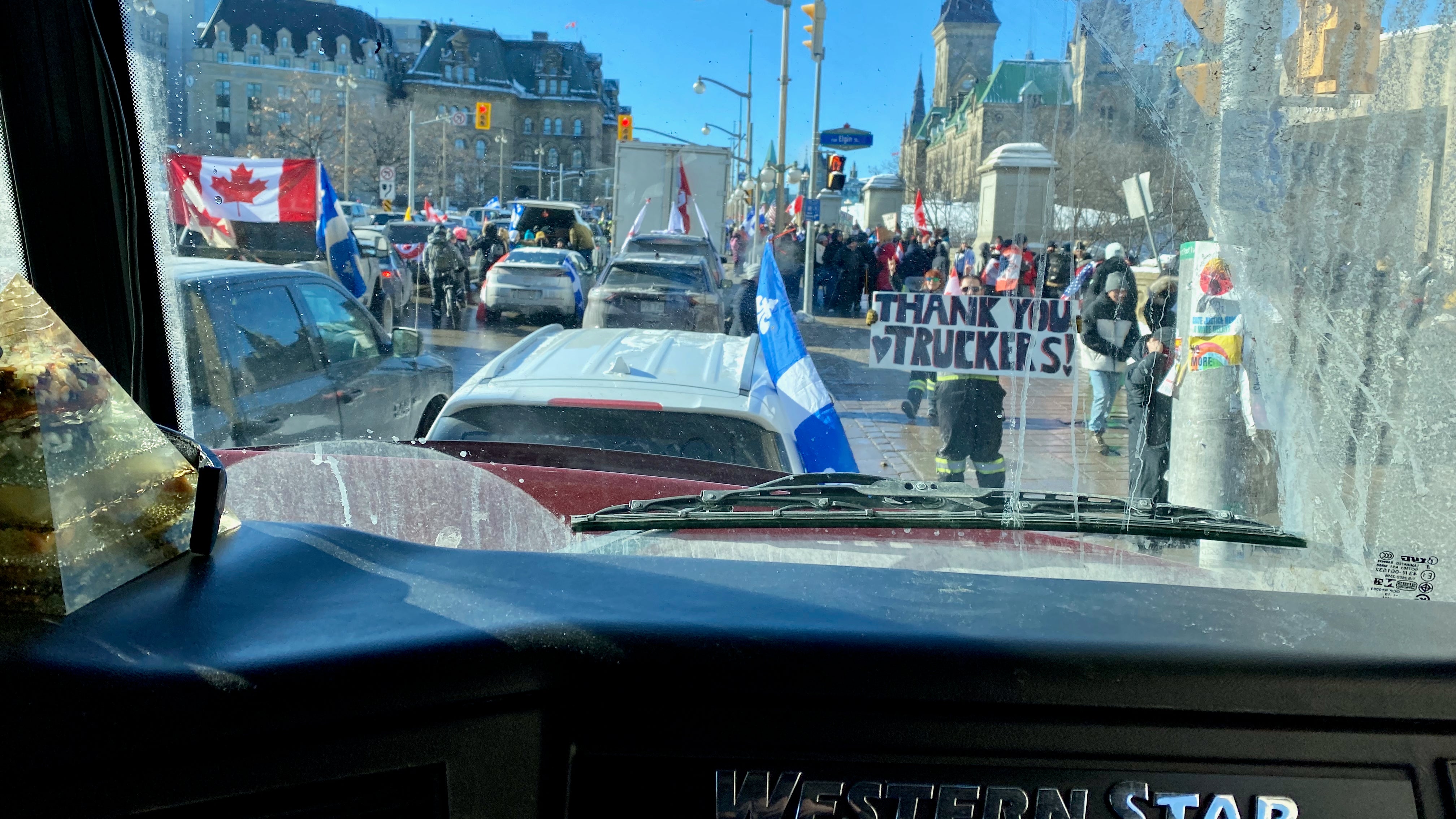 A view from inside a truck as protesters and cars with flags from a convoy make their way through Ottawa.