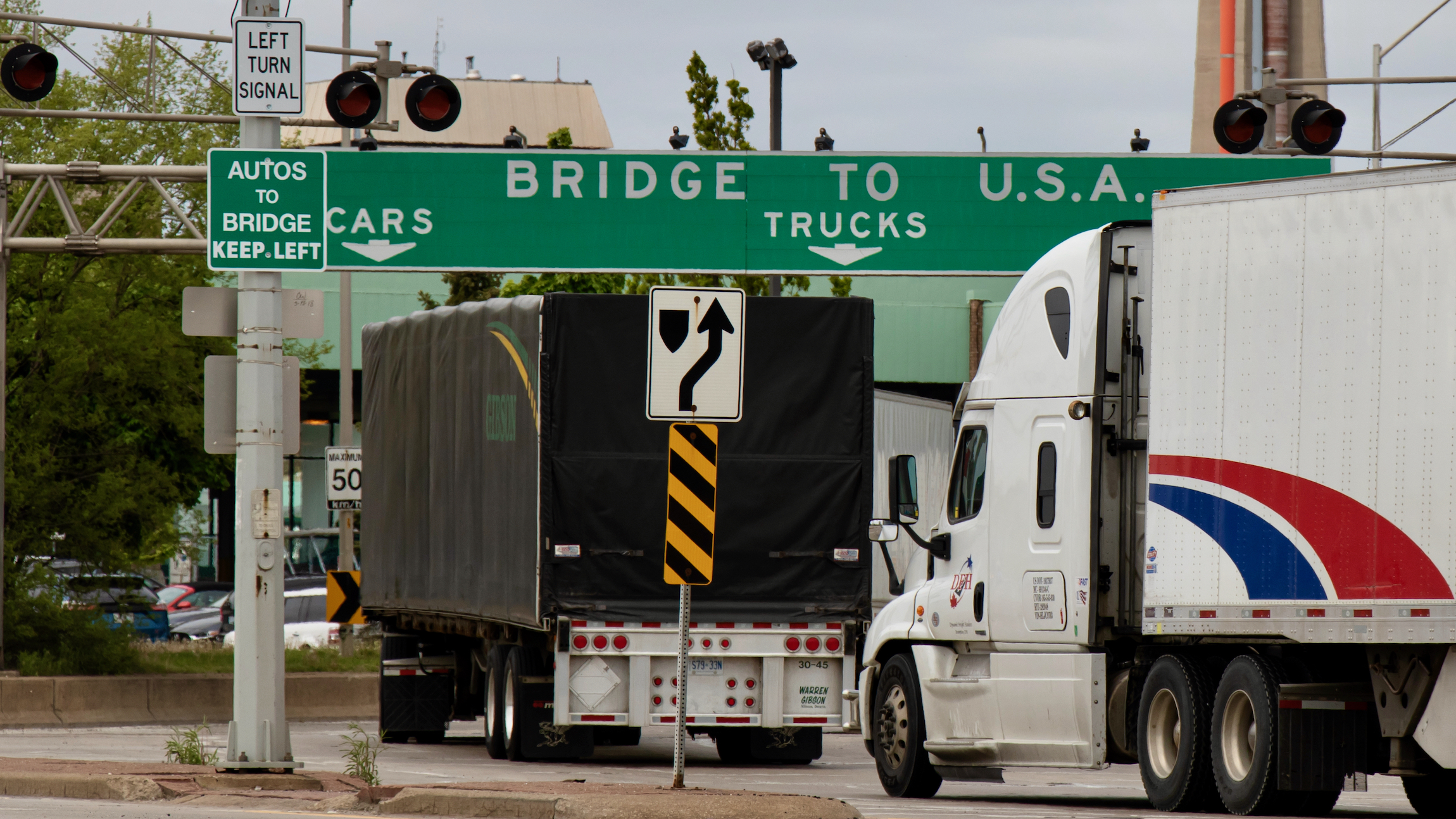 ansport trucks pass under a "Bridge To USA" at the entrance to the Ambassador Bridge, US-Canada border crossing.