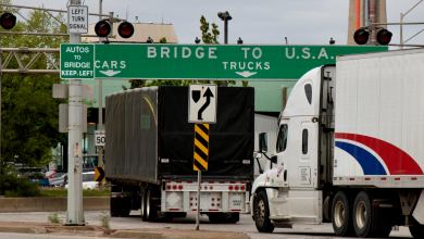 ansport trucks pass under a "Bridge To USA" at the entrance to the Ambassador Bridge, US-Canada border crossing.
