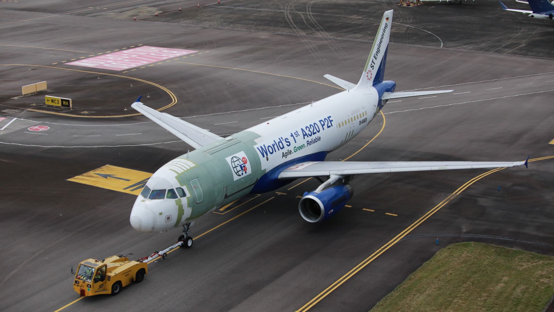 A white plane being towed by a tug with writing on fuselage "World's first A321 P2F"