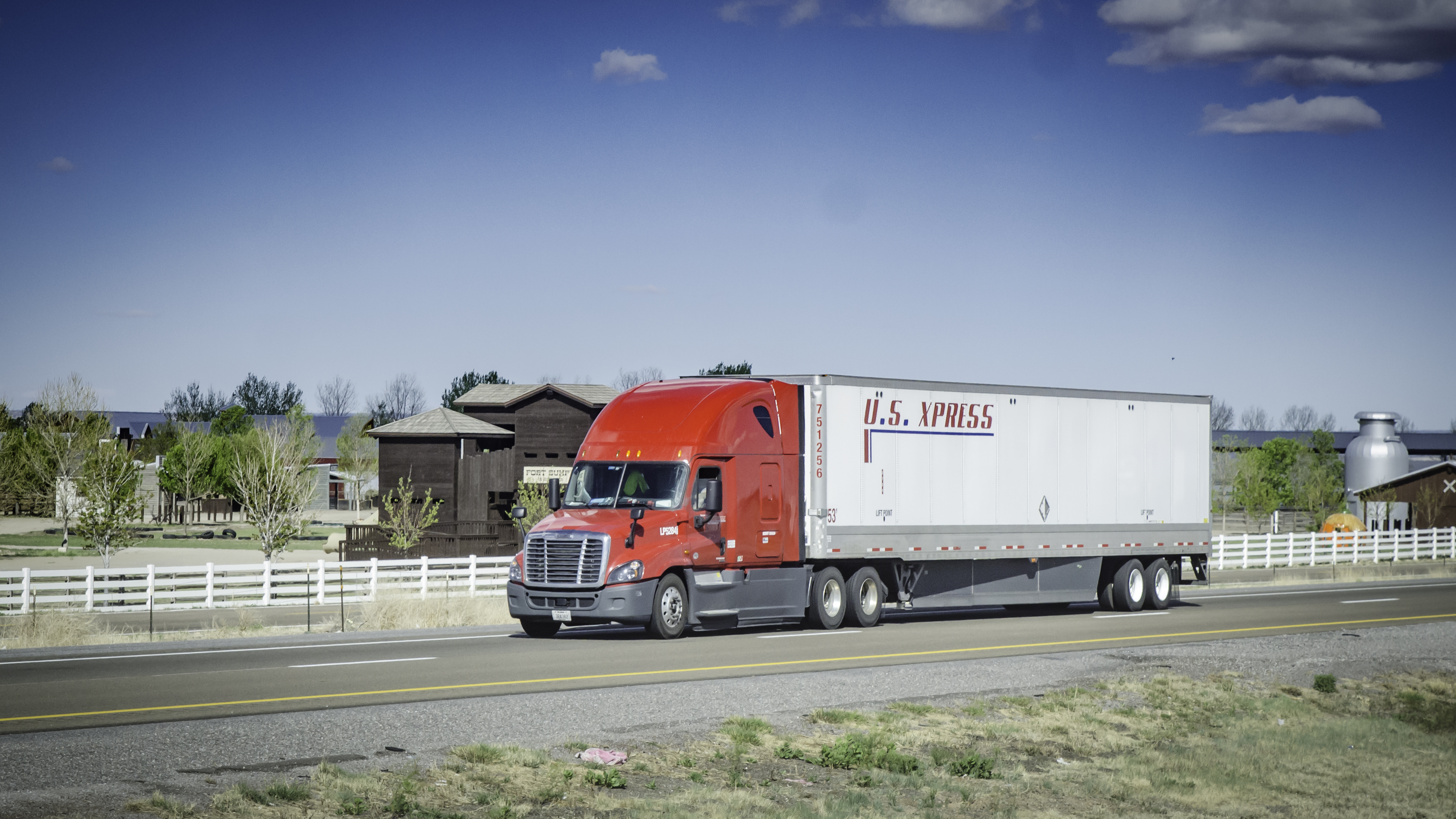 A red and white tractor-trailer of the company US Xpress travels on a road