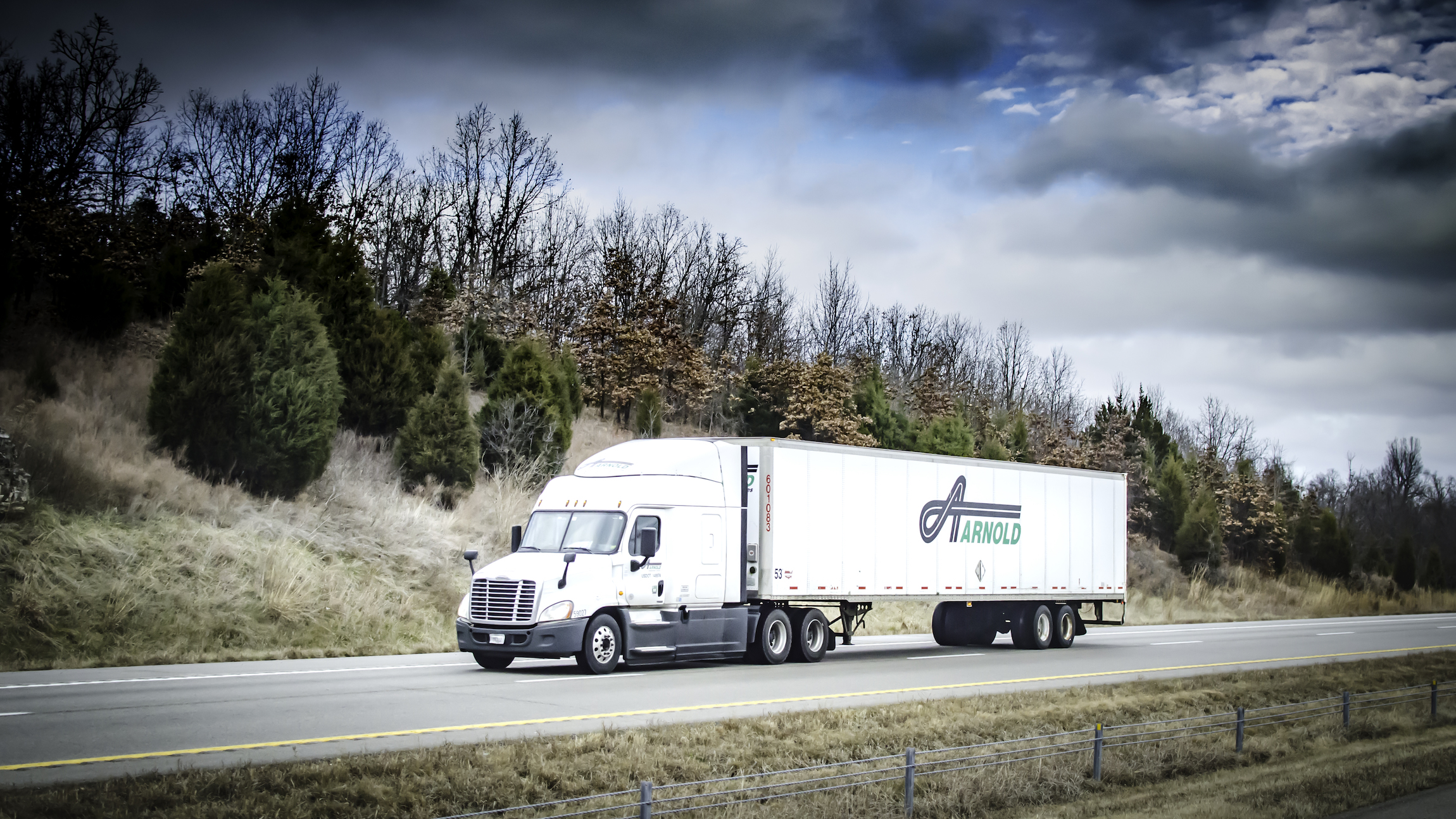 A tractor-trailer with the logo of Texas trucking company Arnold Transporation Services travels on a road seen from the side