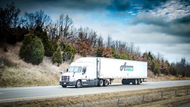 A tractor-trailer with the logo of Texas trucking company Arnold Transporation Services travels on a road seen from the side