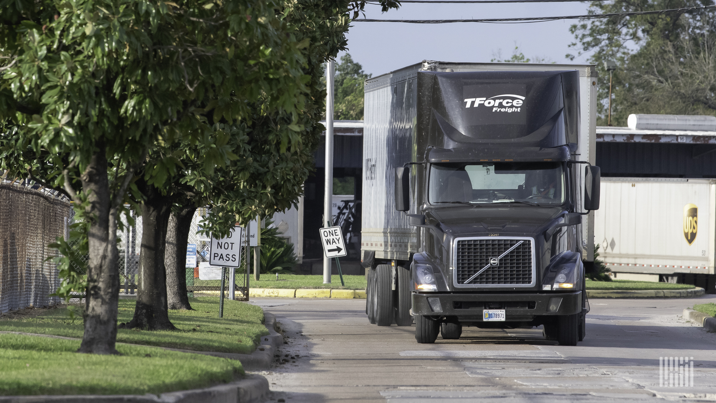 A brown tractor-trailer with the logo of TForce Freight travels on a city street with a trailer of UPS seen in the background.