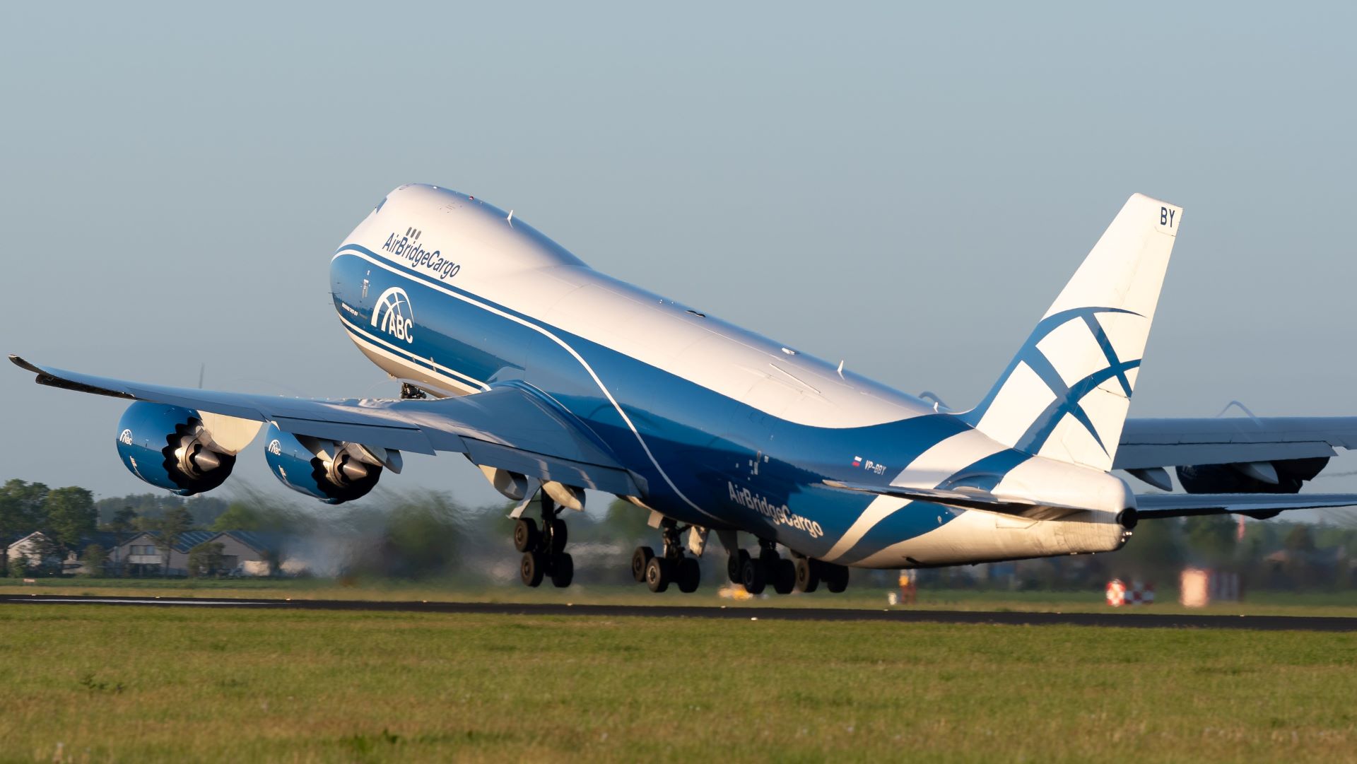 A blue-and-white jumbo cargo jet takes off, view from the rear.