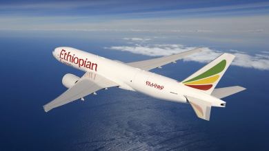A white jet with colorful tail and Ethiopian Airlines logo flies high in the sky, view from above.
