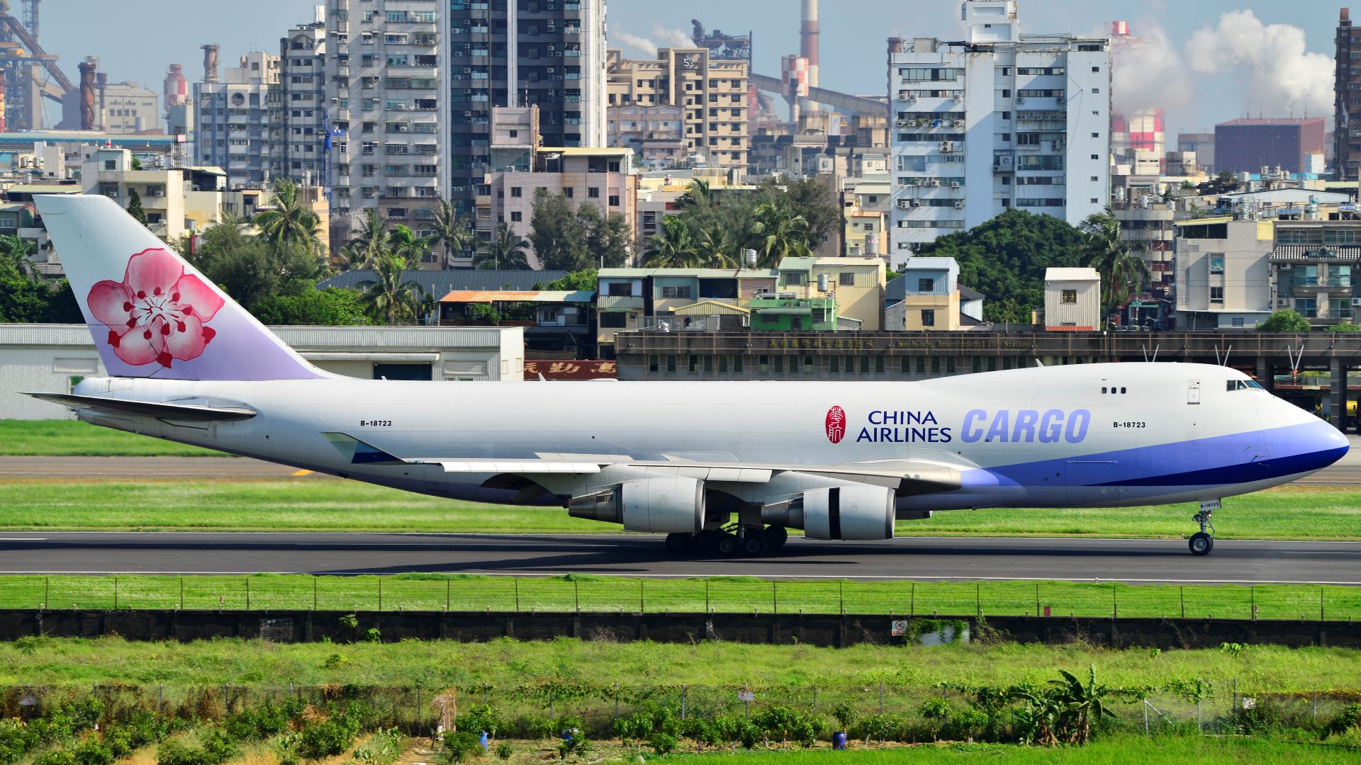 A China Cargo Airlines 747 jumbo freighter with a pink flower on the tail and a light blue color on a runway at a Chinese airport. COVID is hampering airport operations in China now.