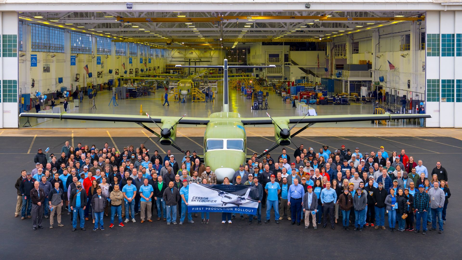 A twin-engine turboprop outside a production hanger with employees celebrating first aircraft rollout.