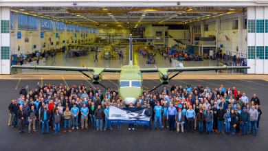 A twin-engine turboprop outside a production hanger with employees celebrating first aircraft rollout.