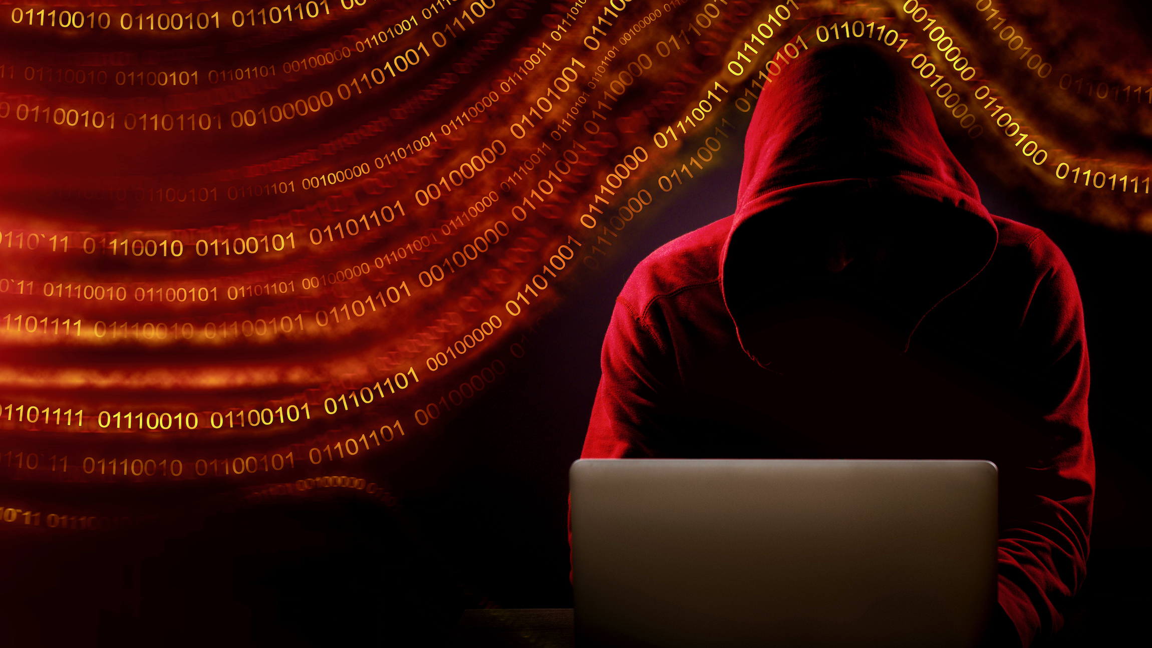A illustration of a man in a hooded sweatshirt, representing a hacker,behind a laptop, illustrating the cybersecurity risks the transport sector