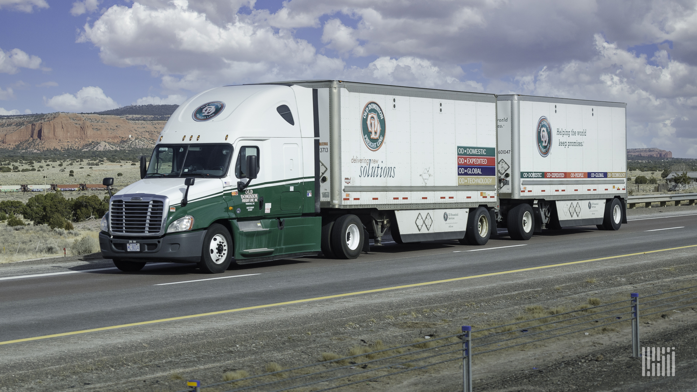 An Old Dominion Freight Line tractor pulling two trailers with train in background