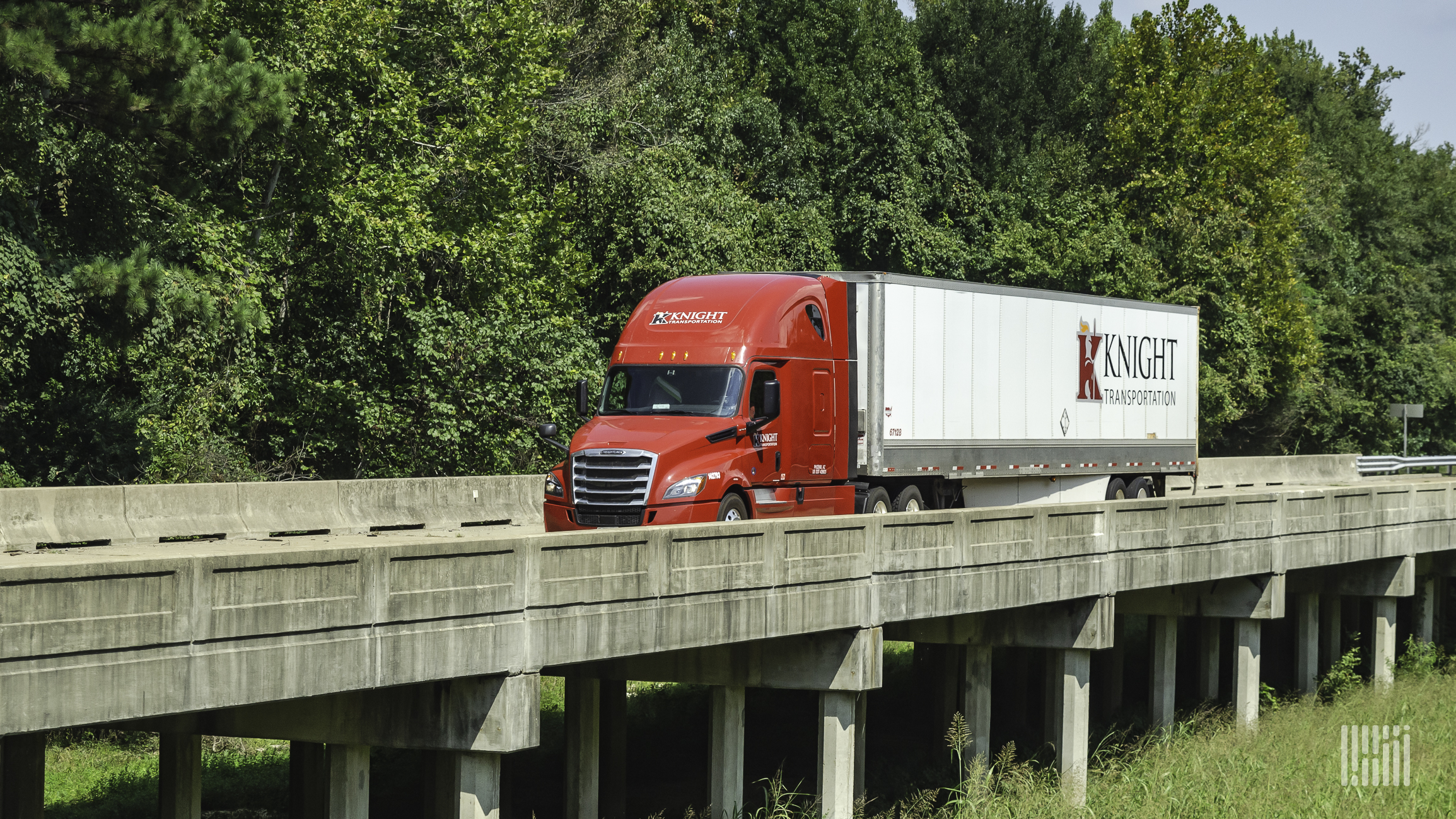 A red Knight-Swift tractor with a white trailer crosses a narrow bridge