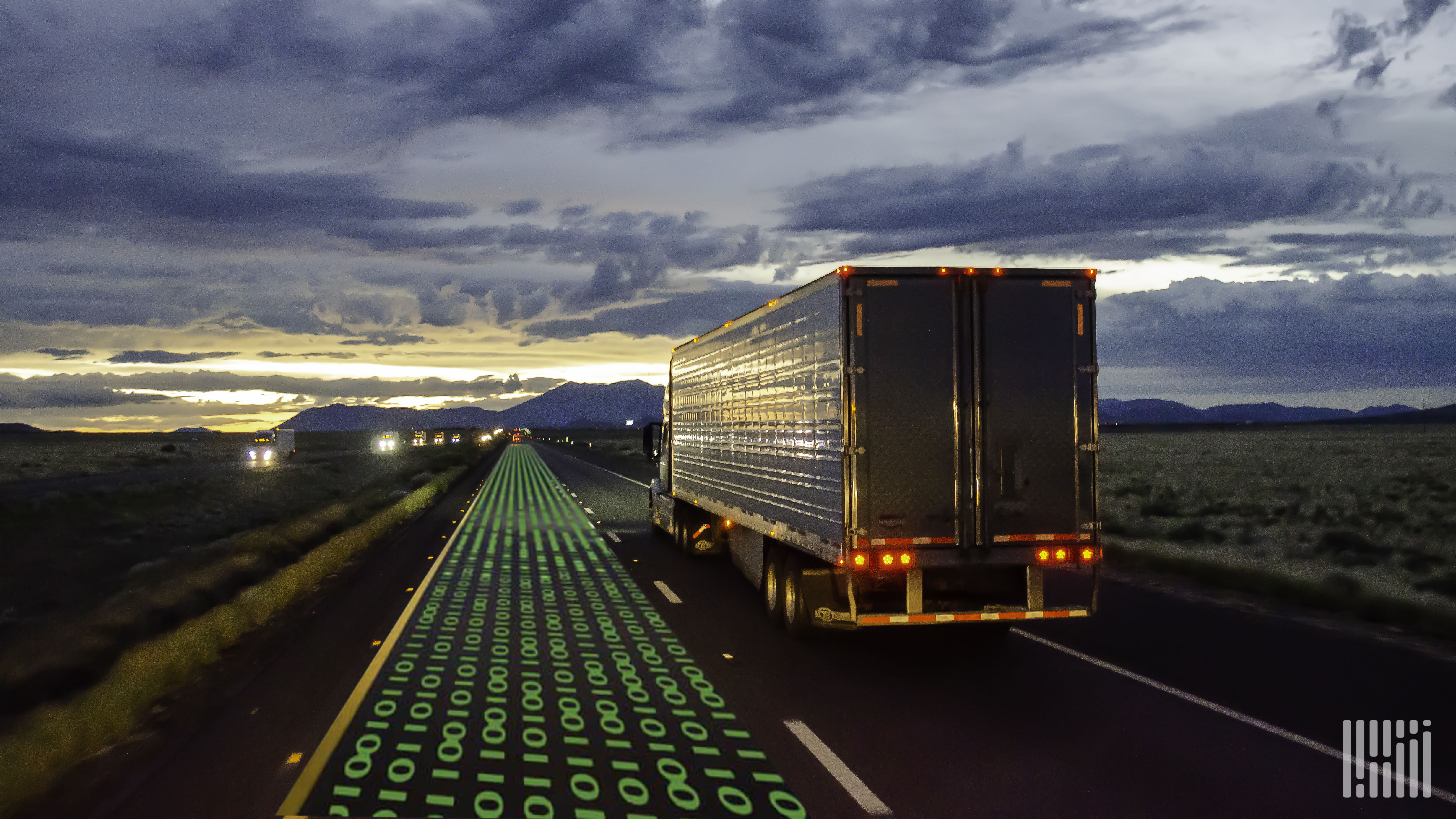 A truck drives along a highway next to a trail of ones and zeros representing automation