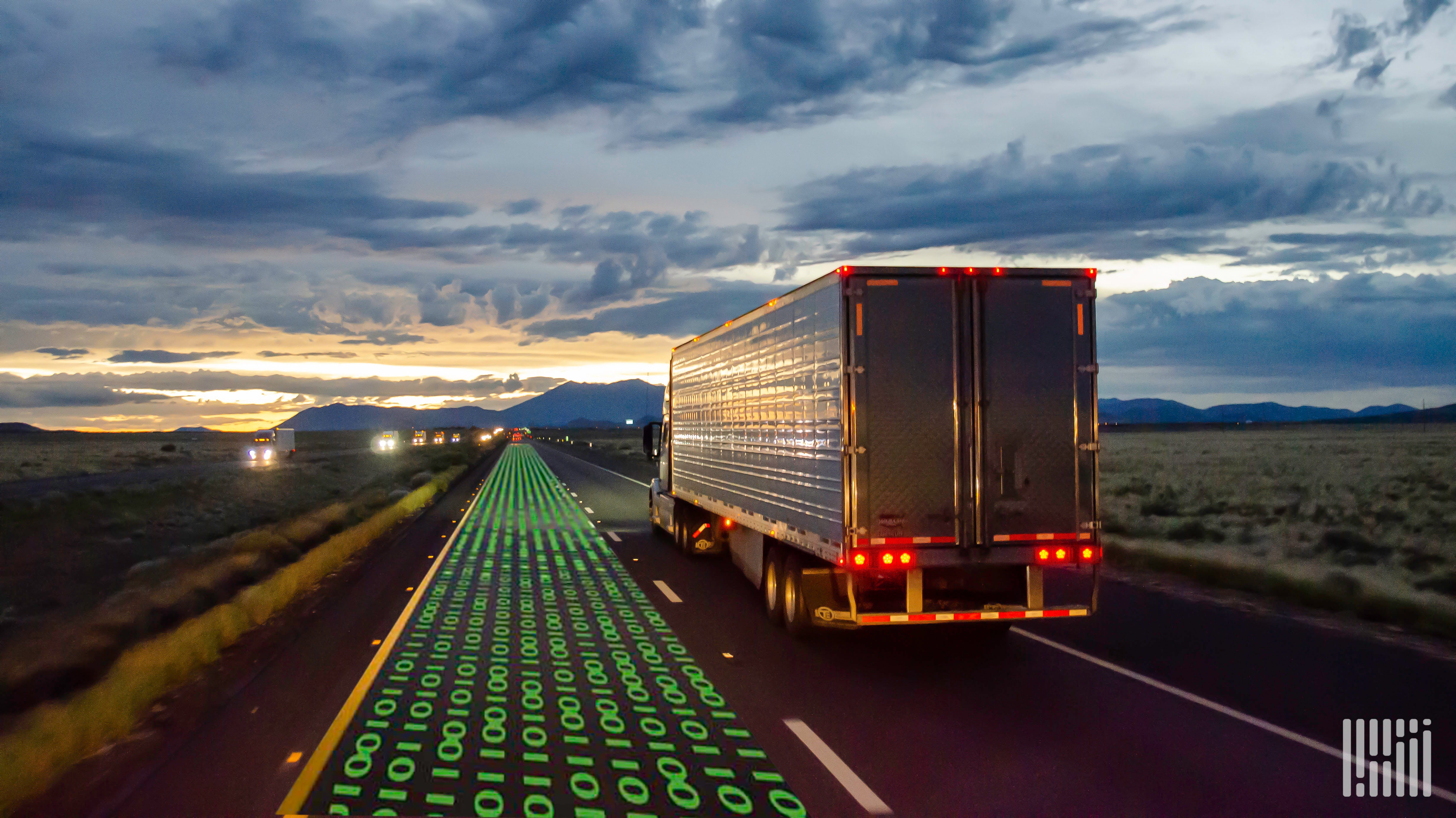 A truck drives along a highway next to a trail of ones and zeros representing automation