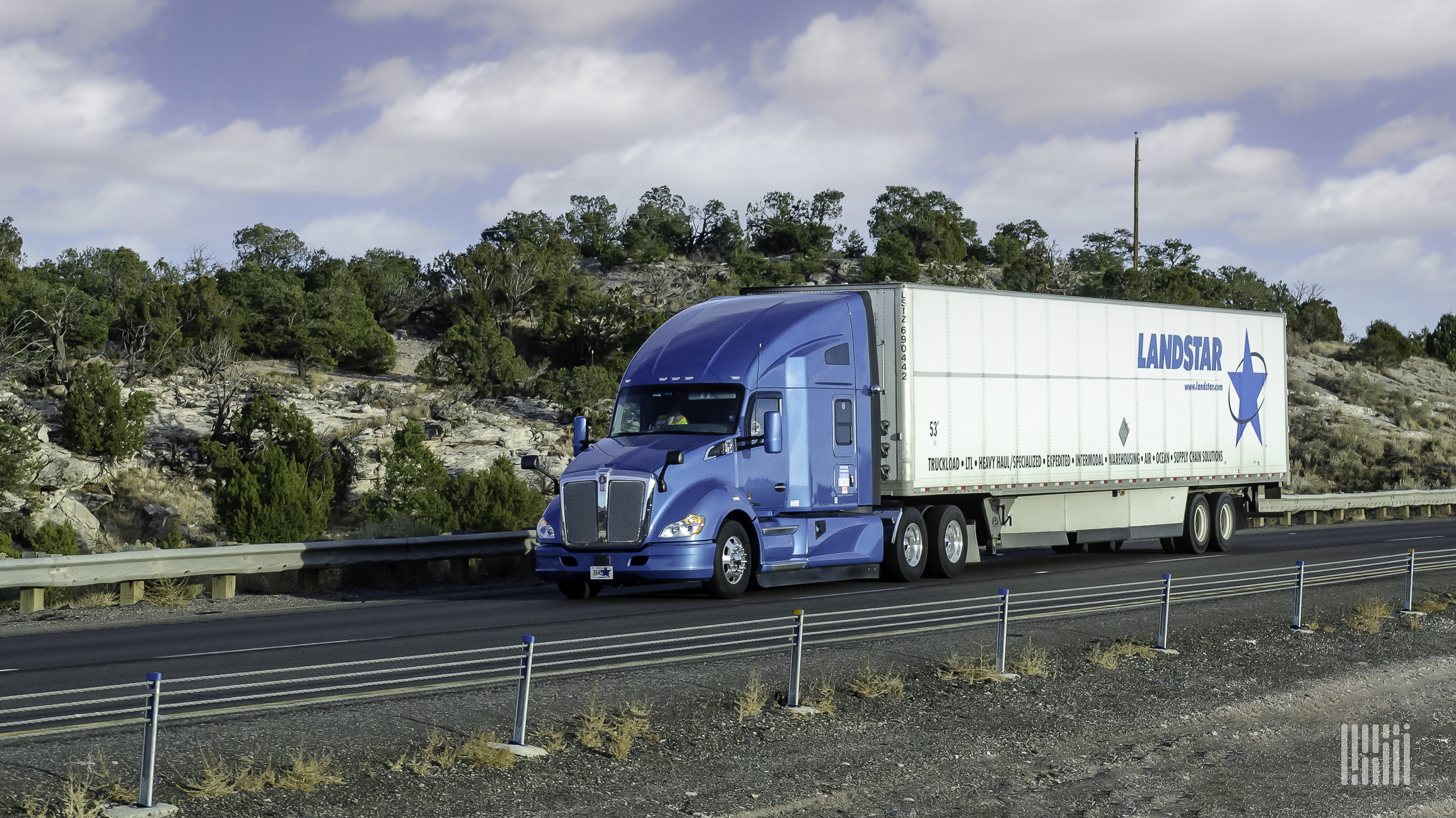 A blue rig hauling a Landstar trailer on the highway