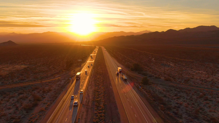 Trucks on a California highway with bright sun on the horizon.