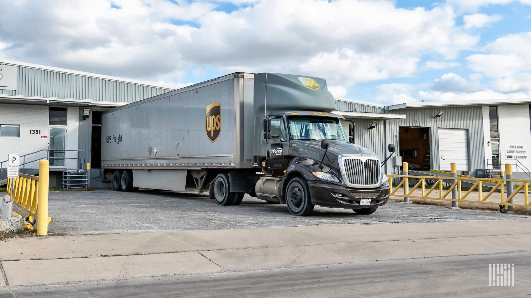 A dark brown tractor-trailer with the logos of TForce Freight and UPS on the tractor, and the logos UPS and UPS Freight on the trailer.