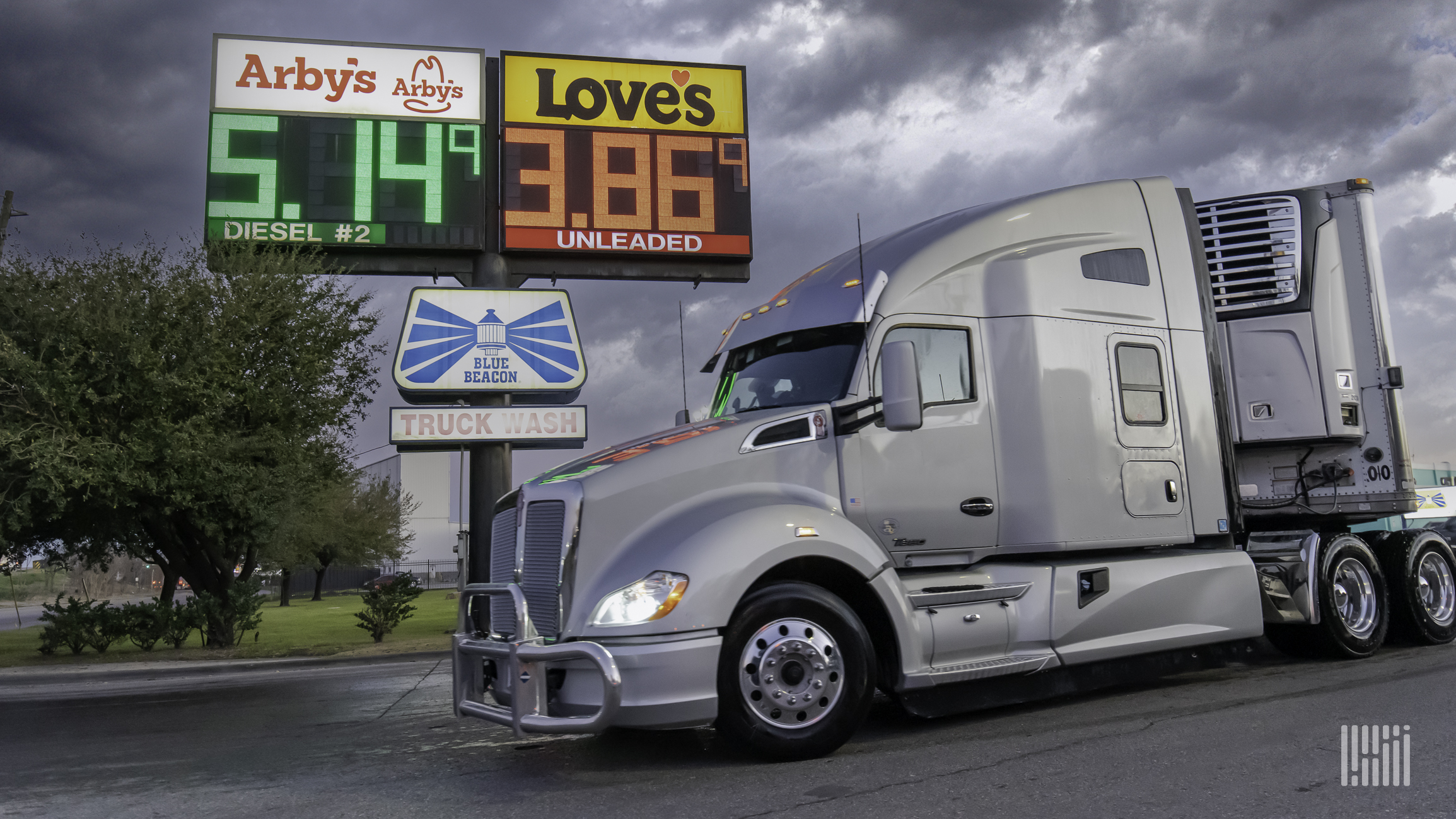 A white semi truck next to a sign showing diesel and regular gas prices