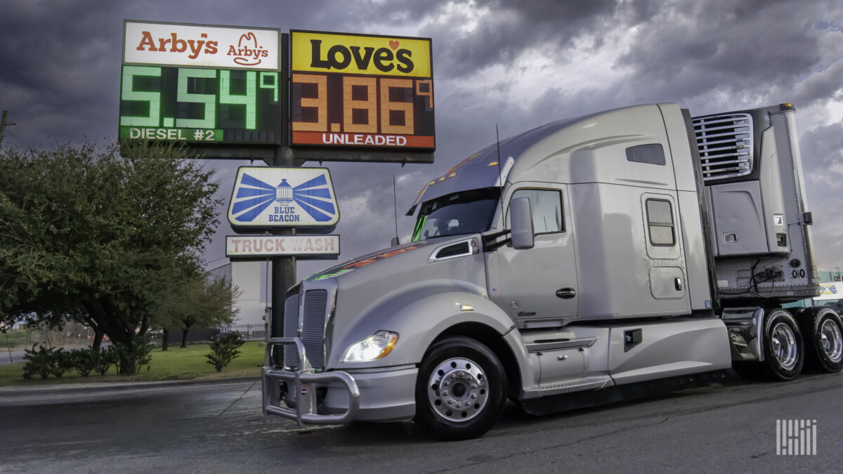 A silver tractor-trailer travels in front of a Love's and Arby's sign with high diesel prices.