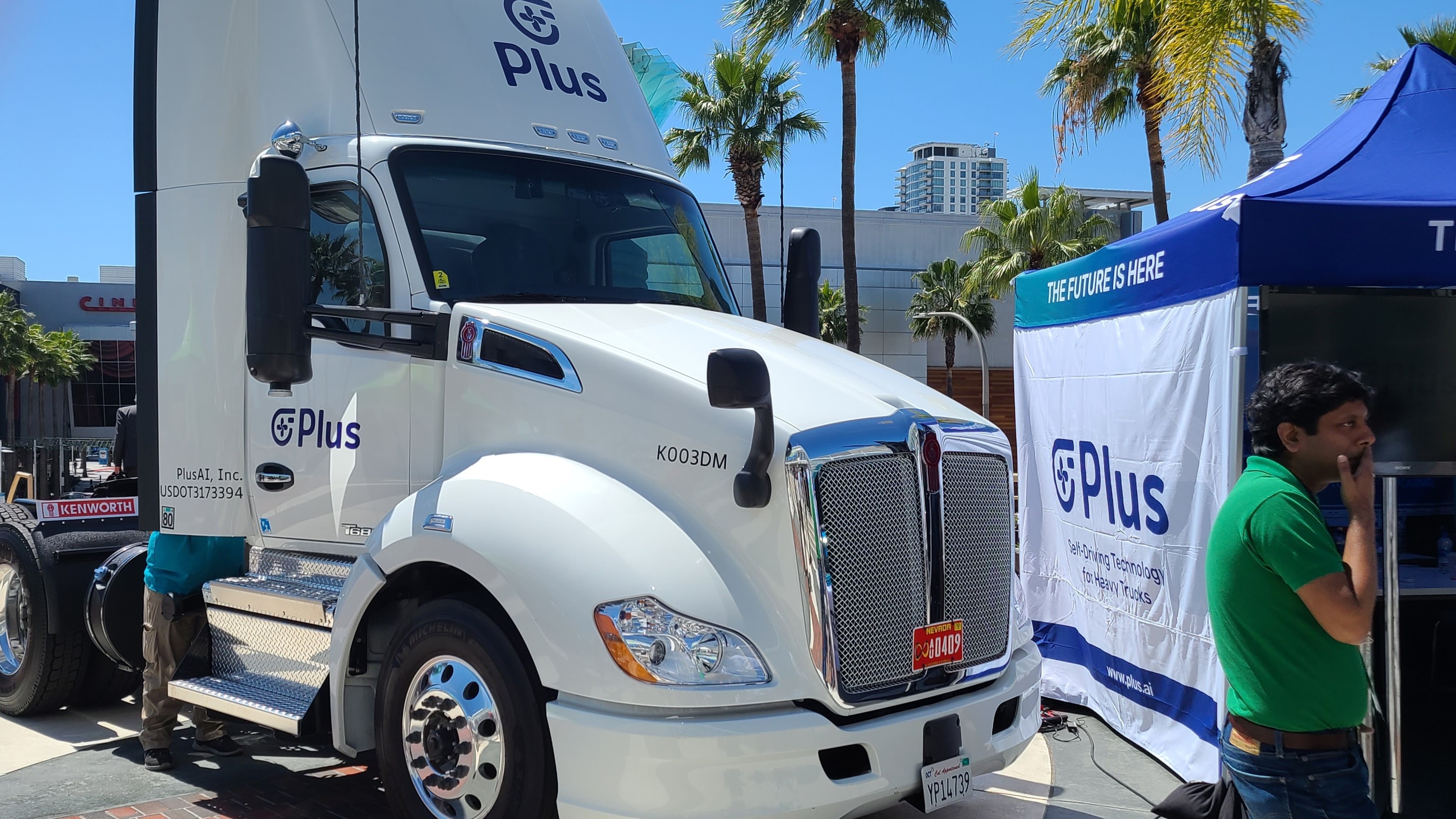 White truck from Plus outside Long Beach Convention Center with palm trees in background.