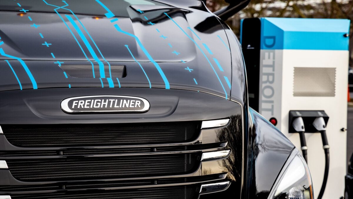 Black Freightliner eCascadia next to blue and white Detroit eFill electric charger