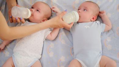 Twin babies on their back being fed from bottles.