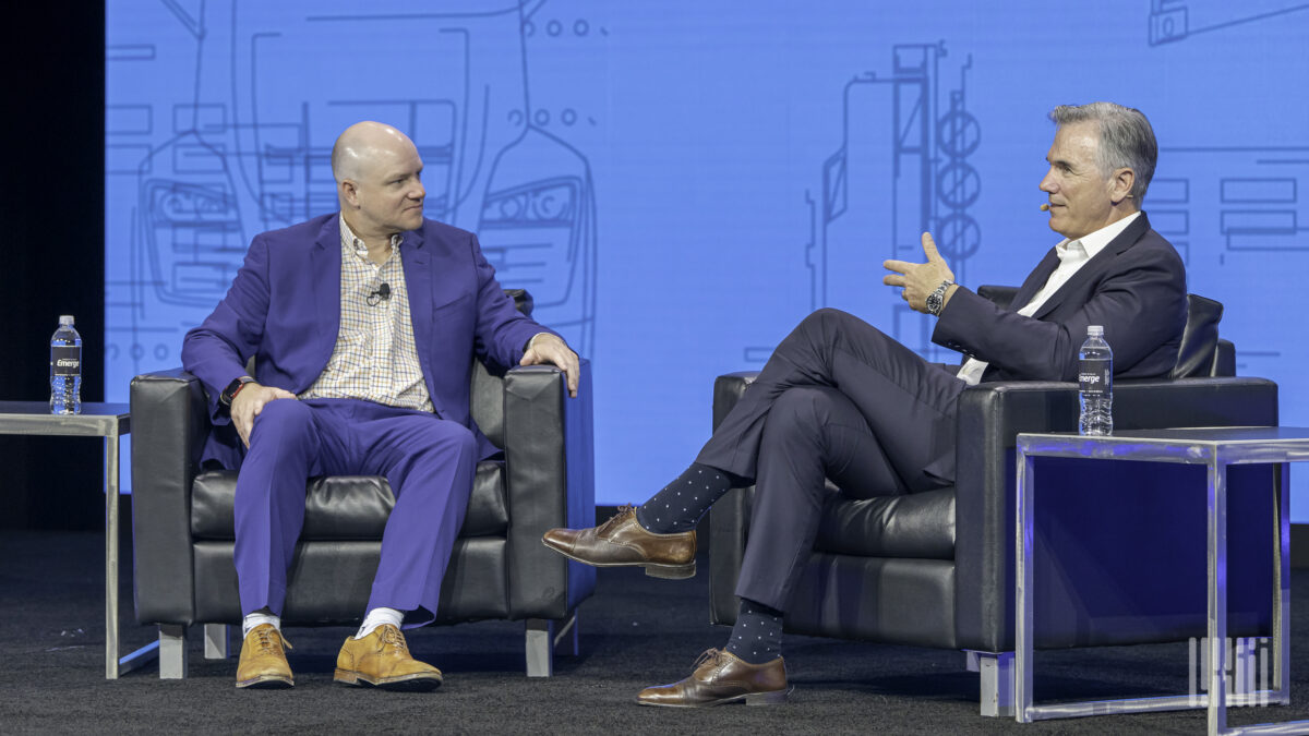 Billy Beane, a man with grey hair and wearing a dark suit, talks to Craig Fuller, a man wearing a blue suit.