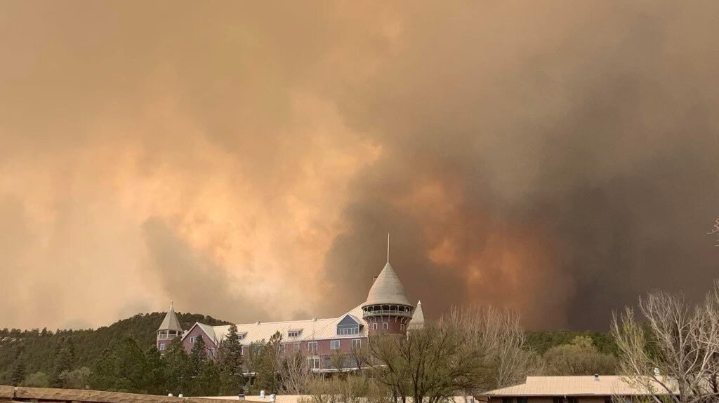 White building in the foreground with a wildfire burning in the background near Las Vegas, New Mexico.
