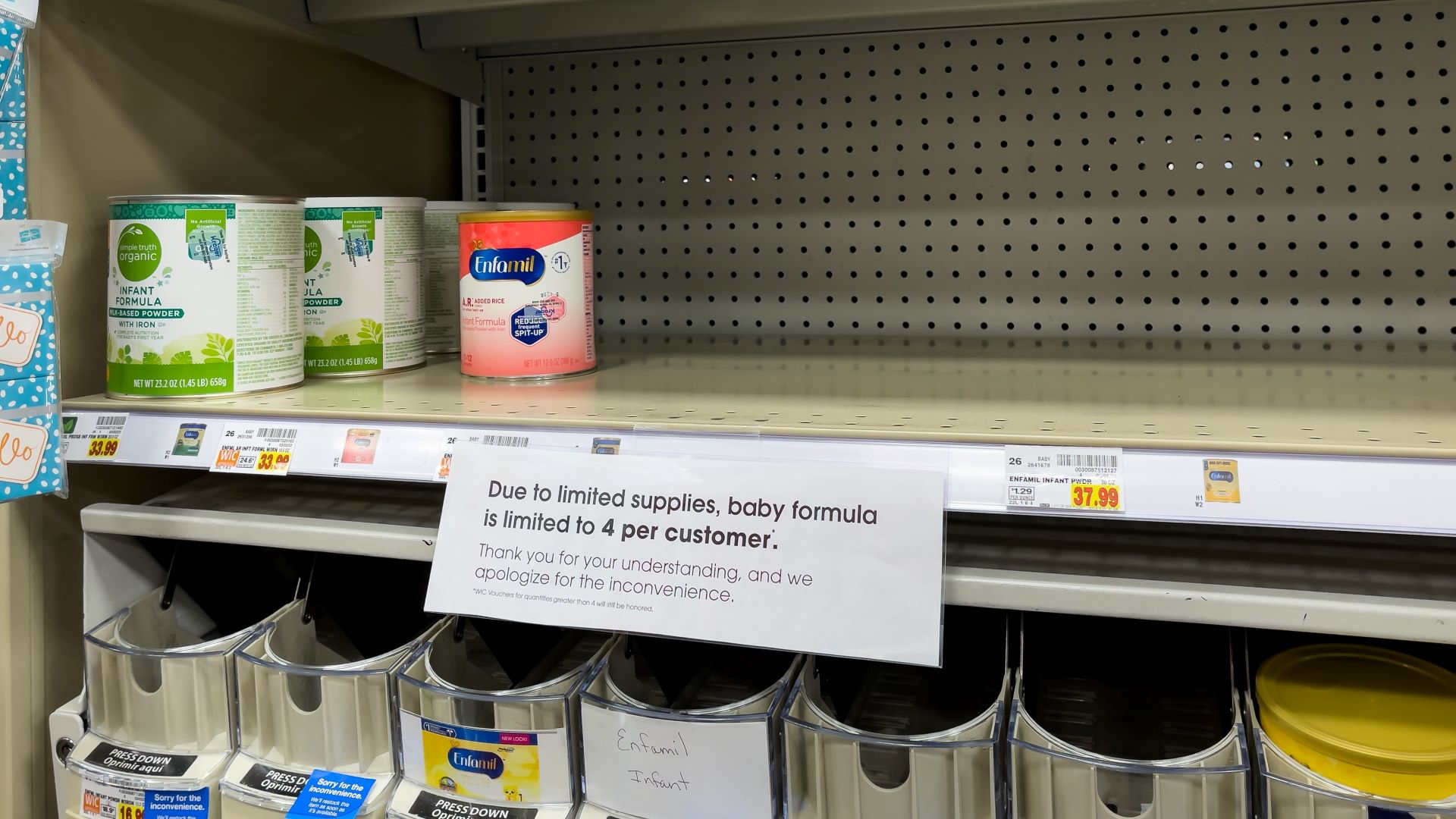 Partially empty shelves of infant formula with a sign alerting consumers.
