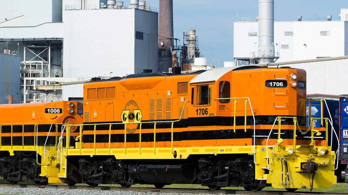 A train on a rail track with intermodal containers in the background.