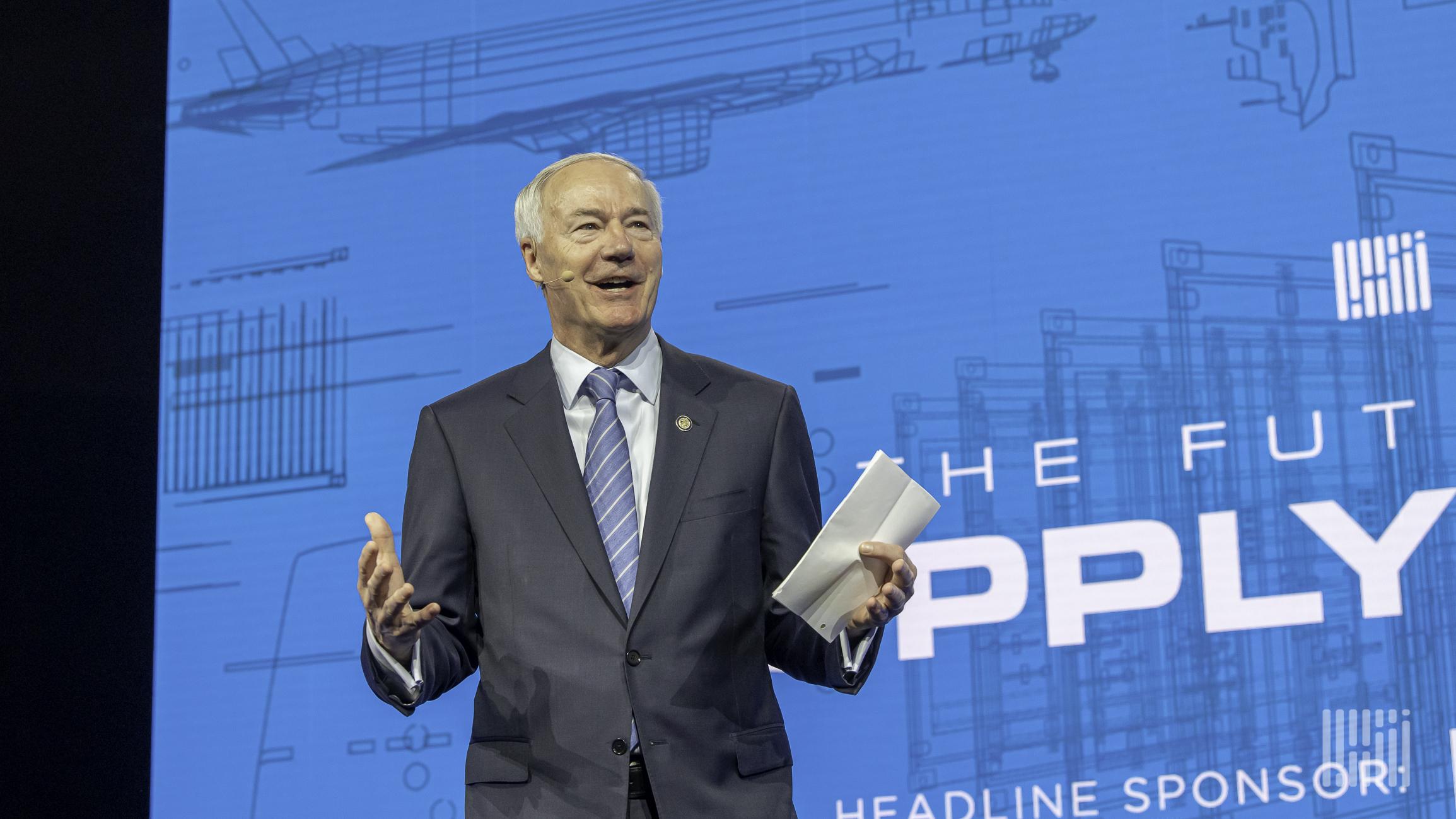 A close-up of Arkansas Governor Asa Hutchinson with arms outstretched talking to an audience.