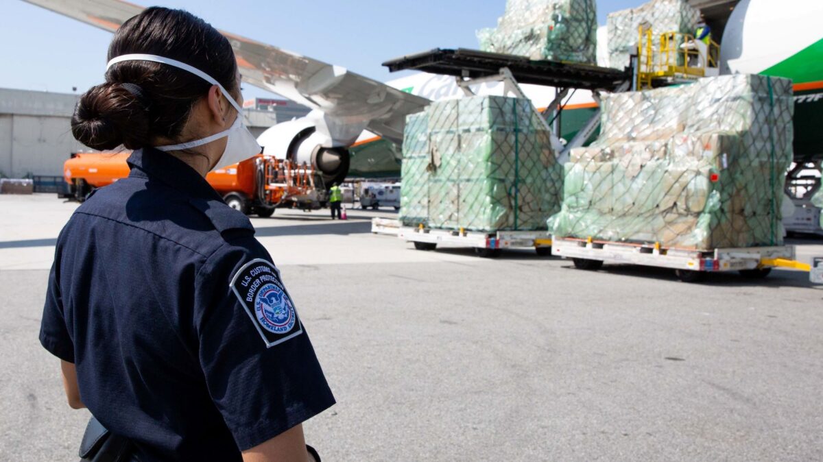 A Customs officer monitors pallets of import cargo unloaded from an aircraft on the tarmac.