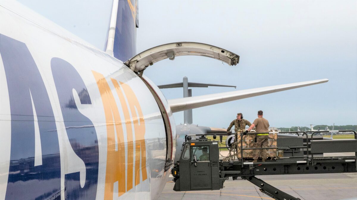 Airmen on a lift hoist by the open door of a cargo plane shipping equipment to Ukraine.