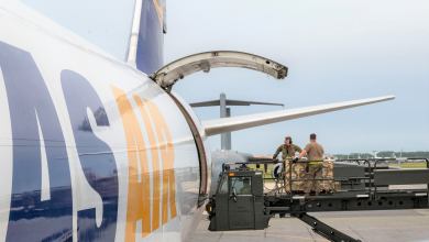 Airmen on a lift hoist by the open door of a cargo plane shipping equipment to Ukraine.
