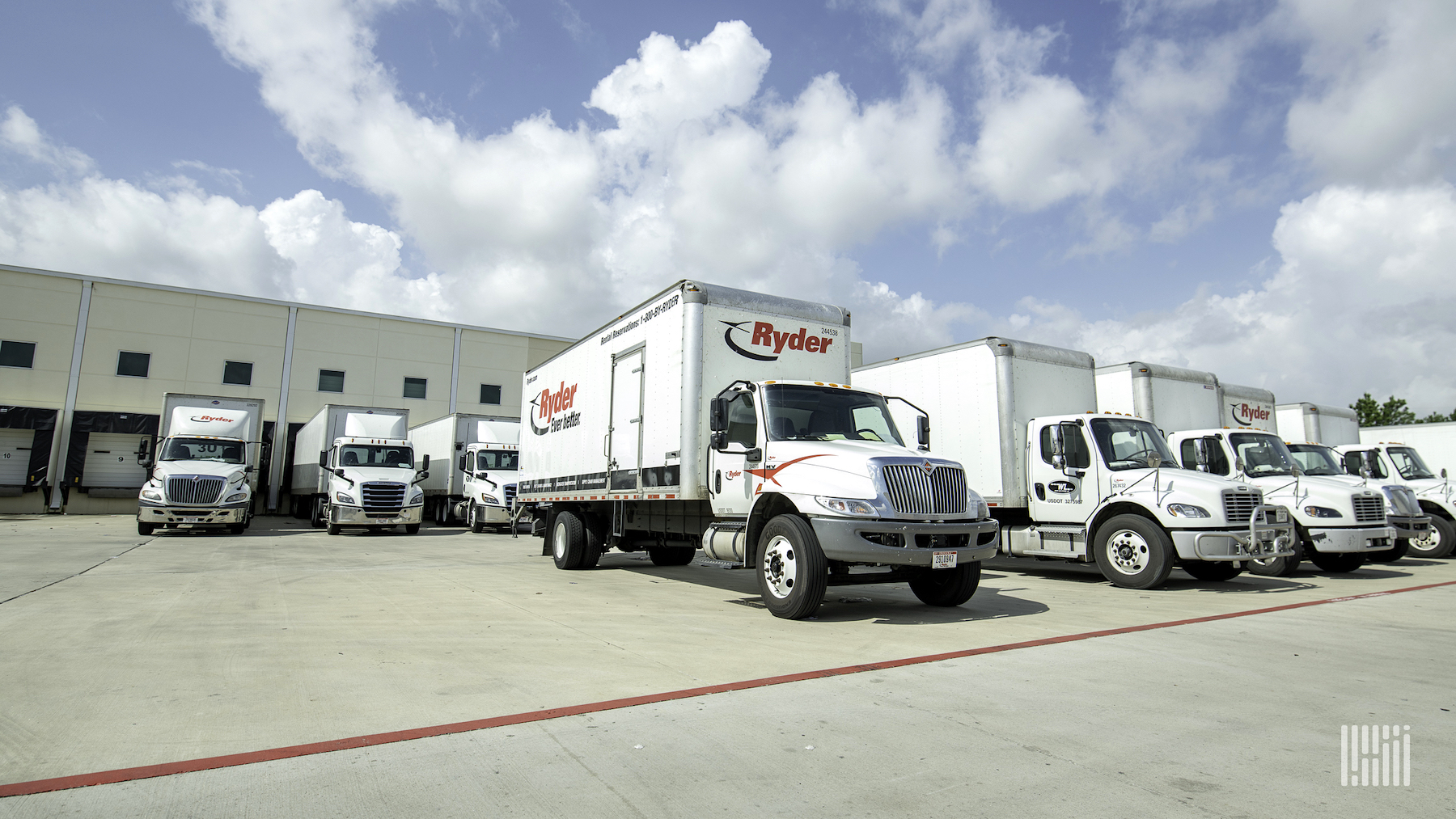 Nine trucks with the logo of Ryder written on them are parked at a facility