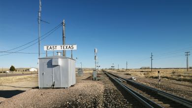 A photoraph of a rail track in a desert-like field. A small building with a sign that says East Texas is next to the track.