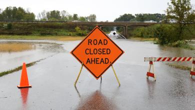 Orange "Road Closed Ahead" sign near flooded highway.