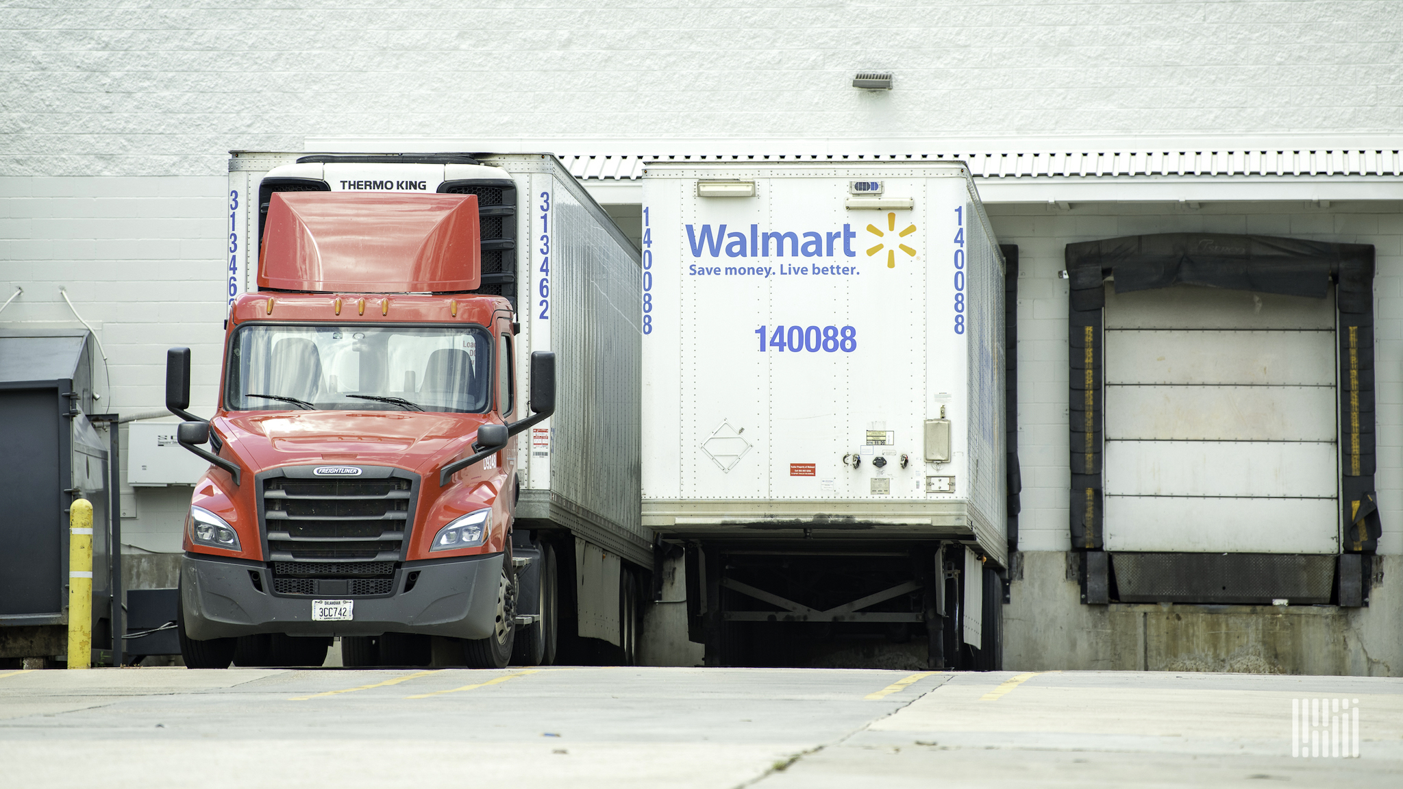 A red semi-truck next to a white Walmart trailer docked at loading facility