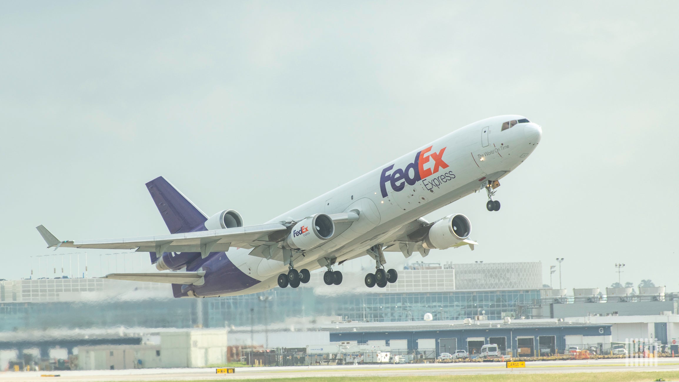 A purple and white FedEx plane lifts off from runway.