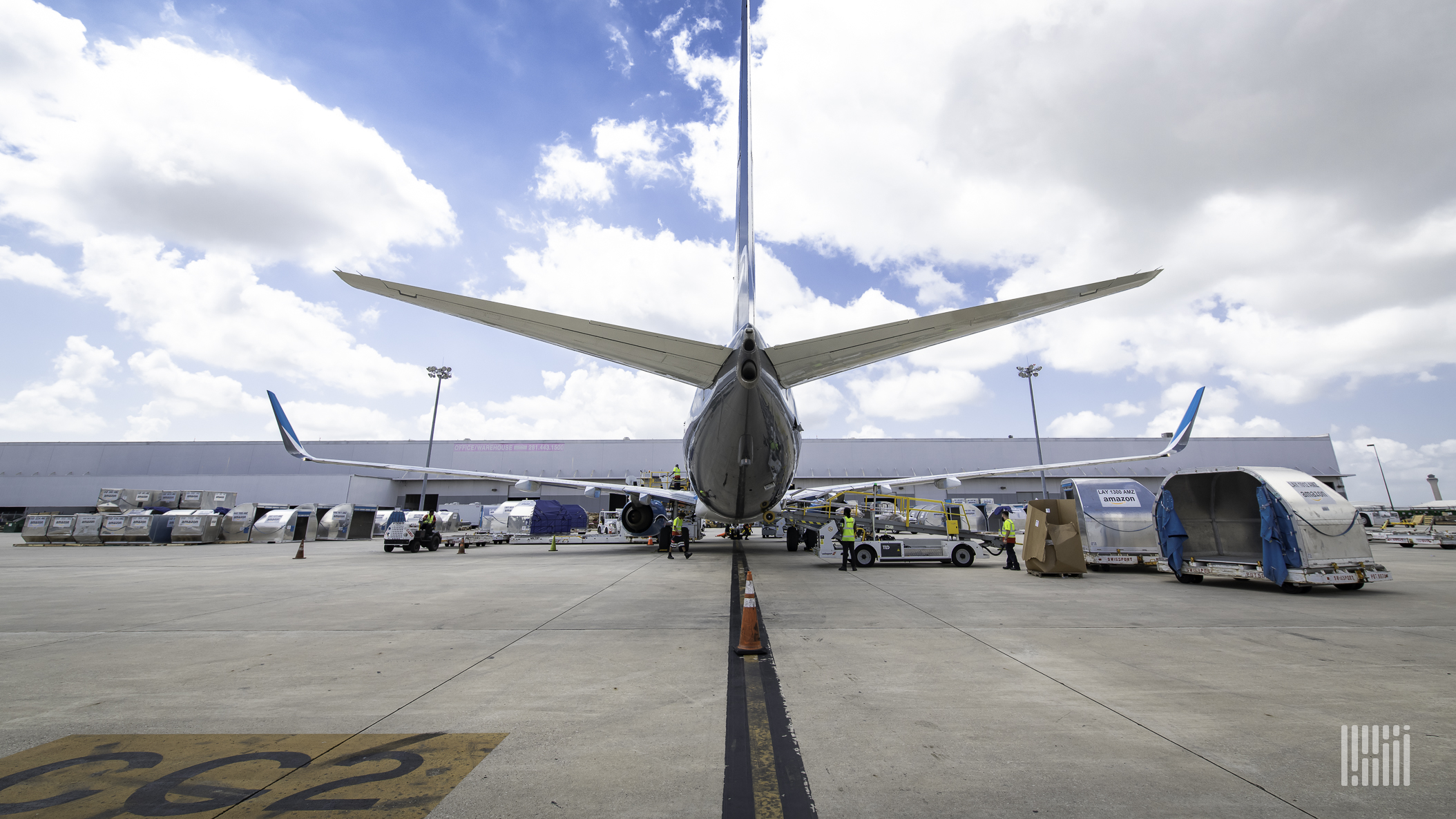 Rear view of a commercial jet parked at the terminal with a cargo container sitting on the tarmac.