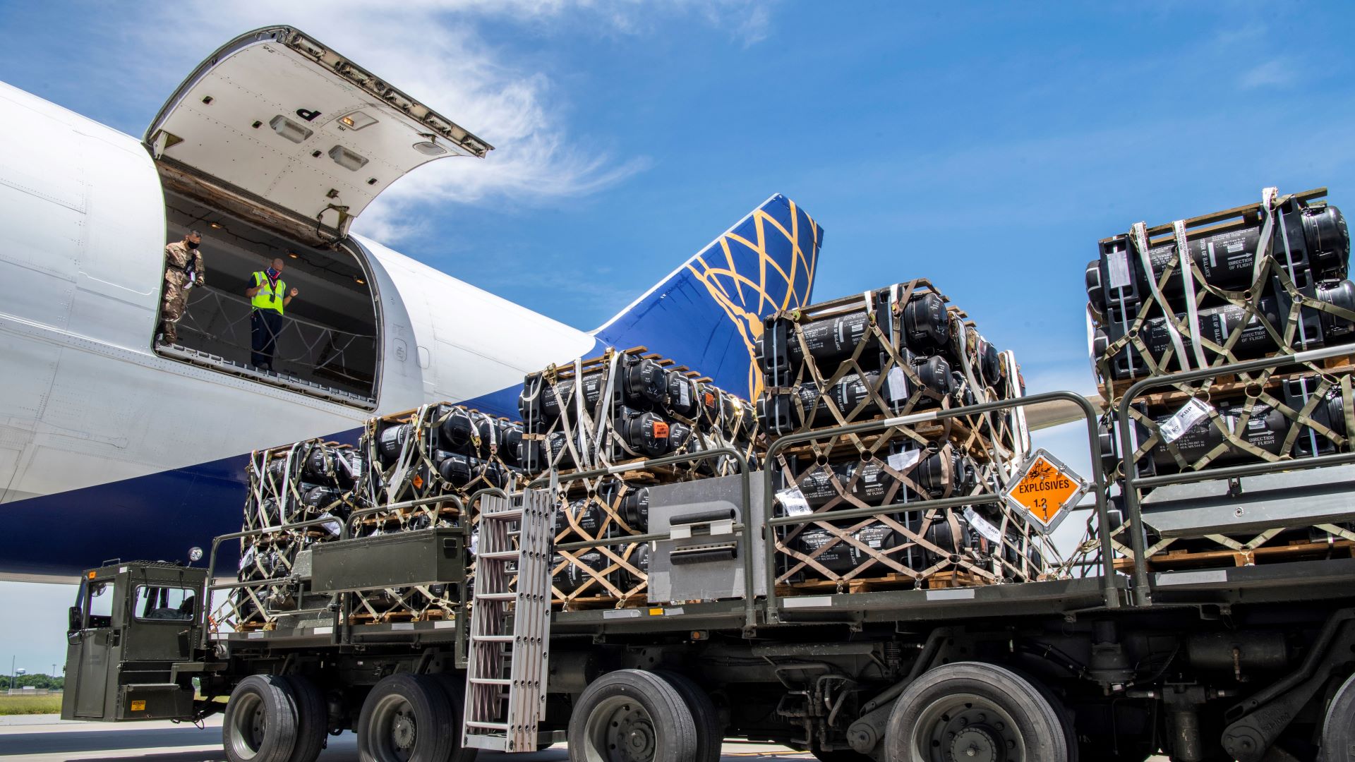 A military flatbed truck delivers missiles to load on a a white United Airlines jet with the cargo door open.