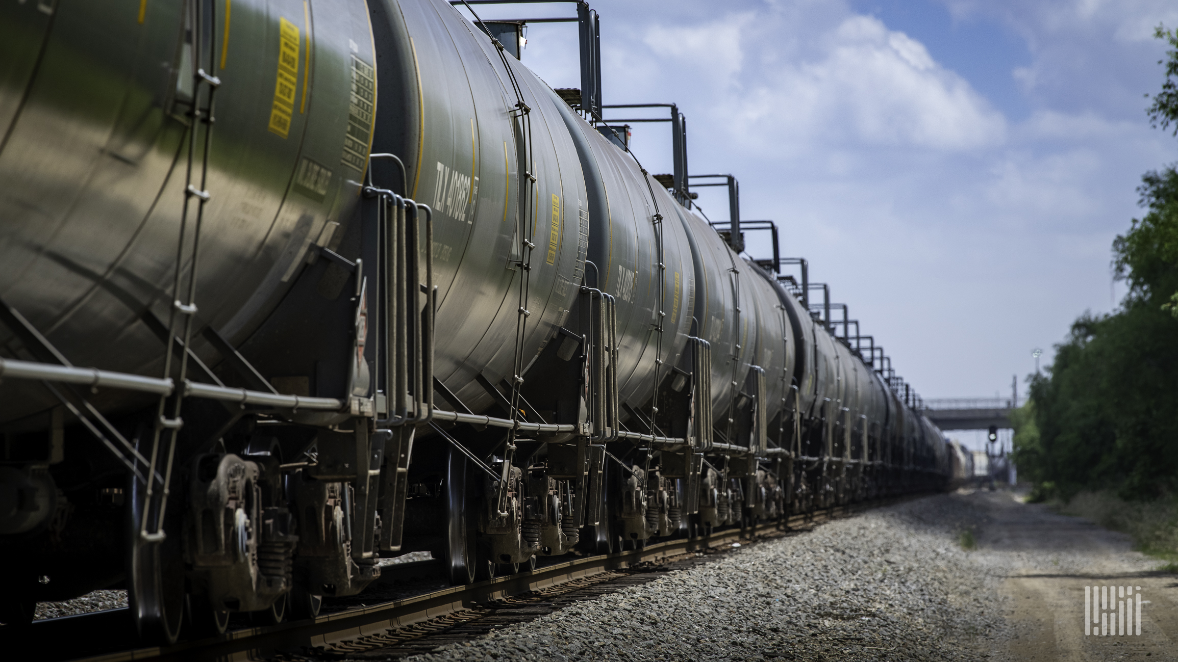 A train of tank cars travels down a rail track.