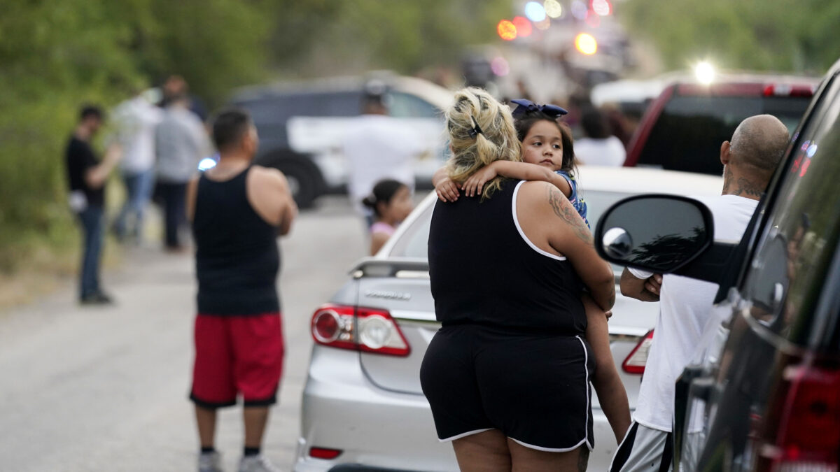 Onlookers stand near the scene where a tractor-trailer packed with dozens of bodies was discovered on Monday in San Antonio