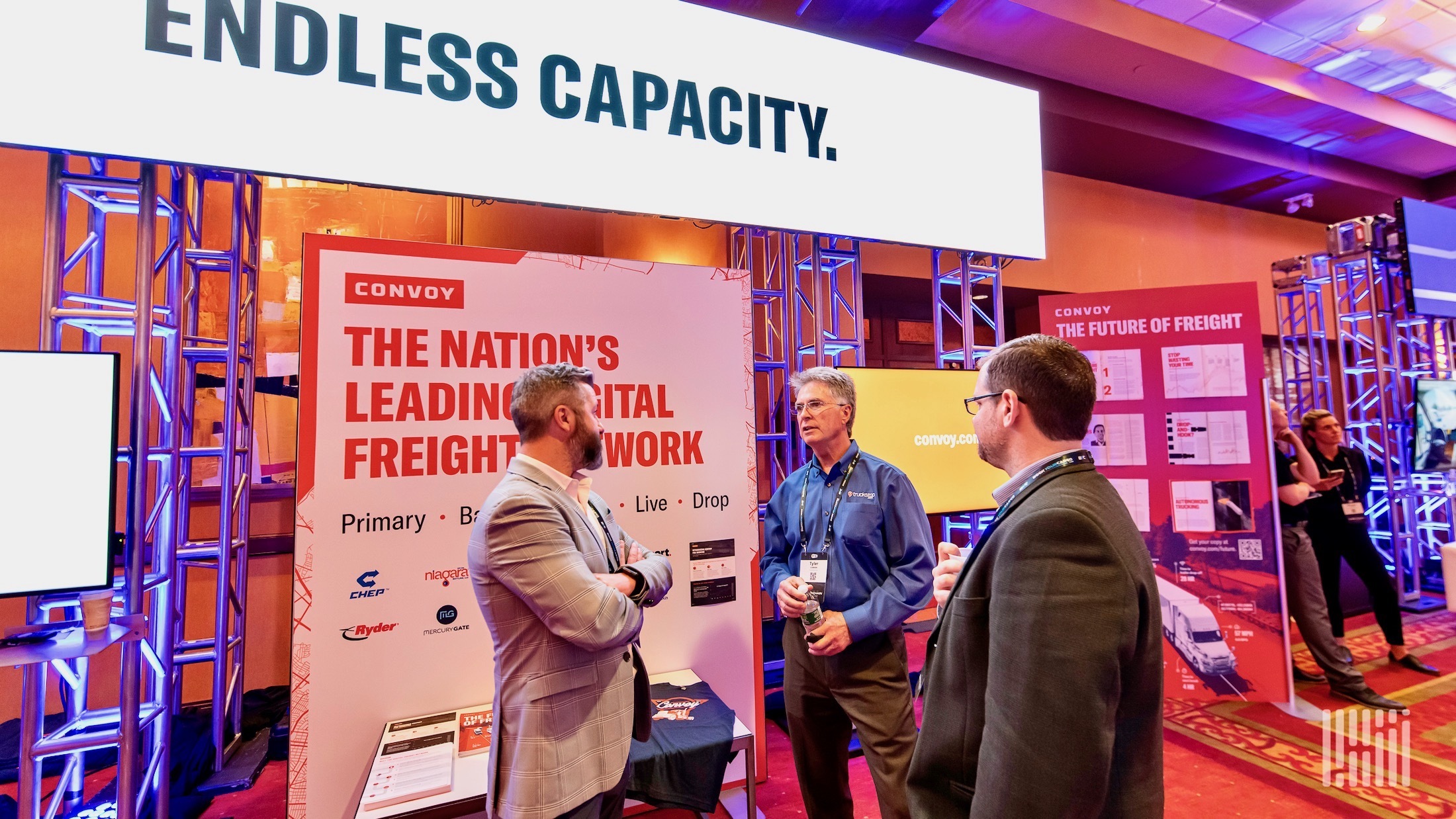 People stand in front of a Convoy booth at a trade show.