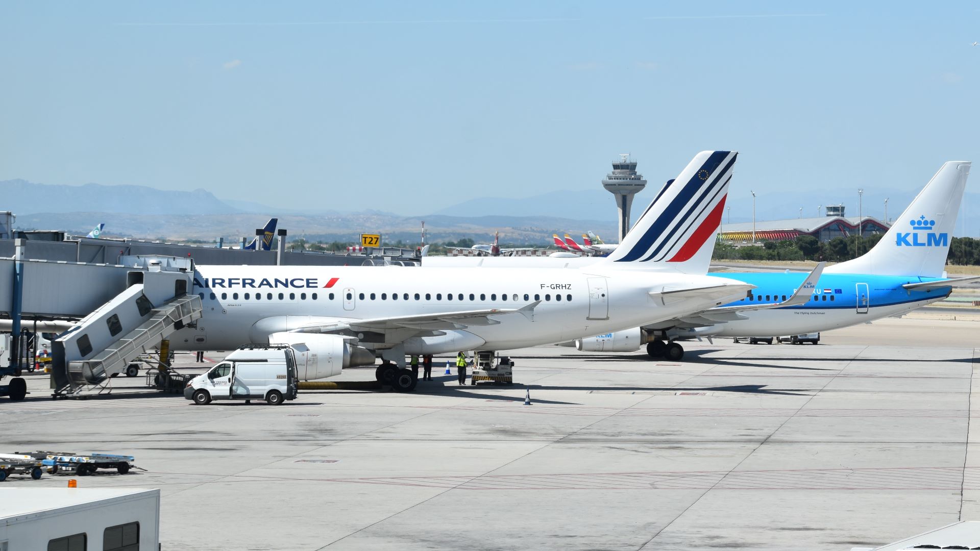 A baby blue KLM plane and an red, white and blue Air France plane parked at a passenger terminal.