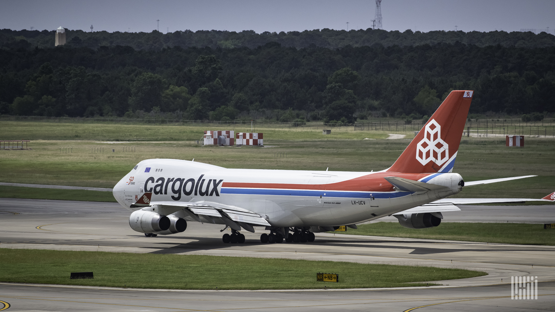 A white Cargolux jumbo jet with red tail prepares to take off. View from the rear.