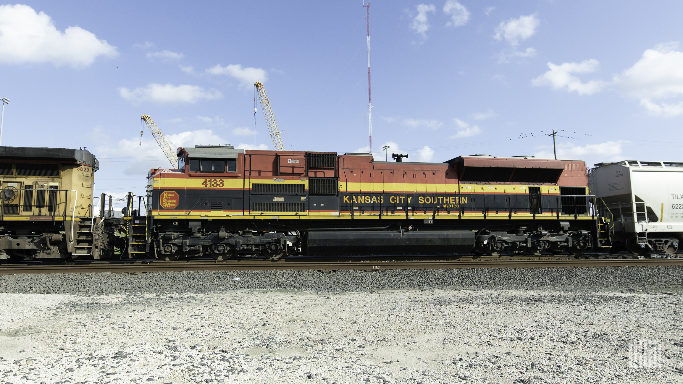 A train that says Kansas City Southern on its side is parked at a rail yard.