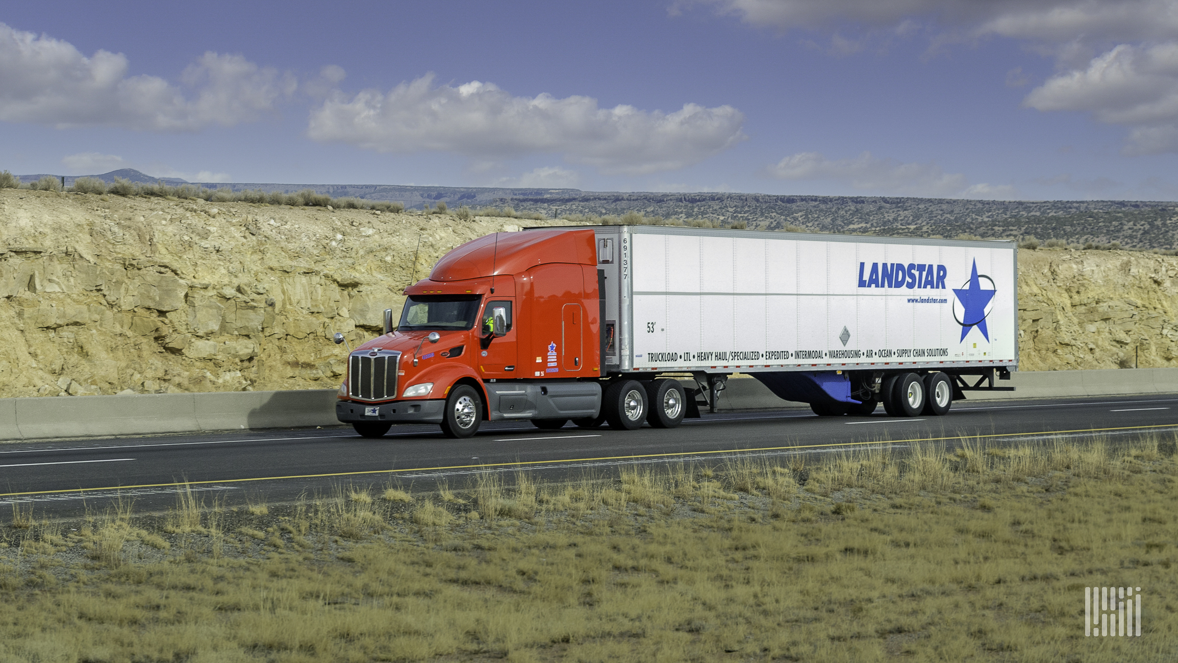 A Landstar trailer being pulled by a red tractor