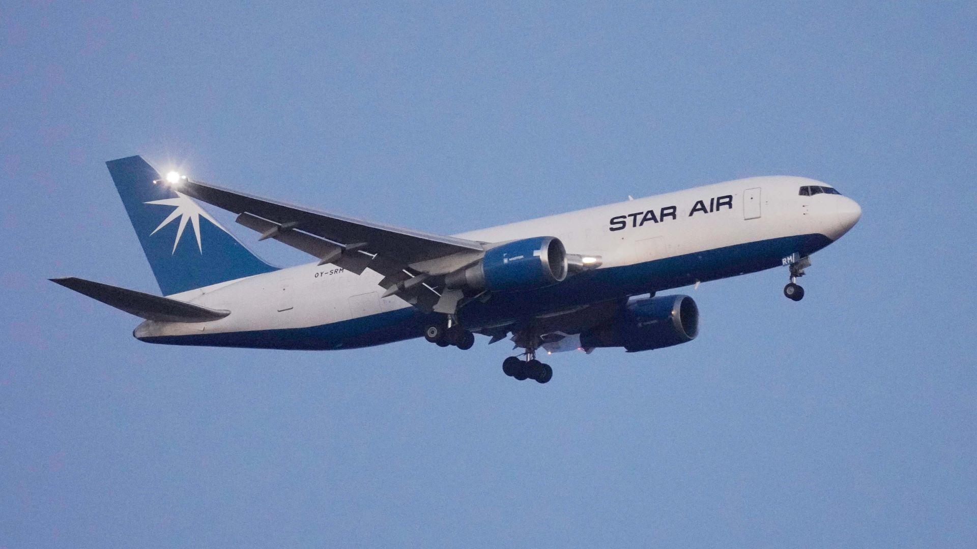 A white Star Air cargo jet with blue tail in sky with wheels down to land soon.